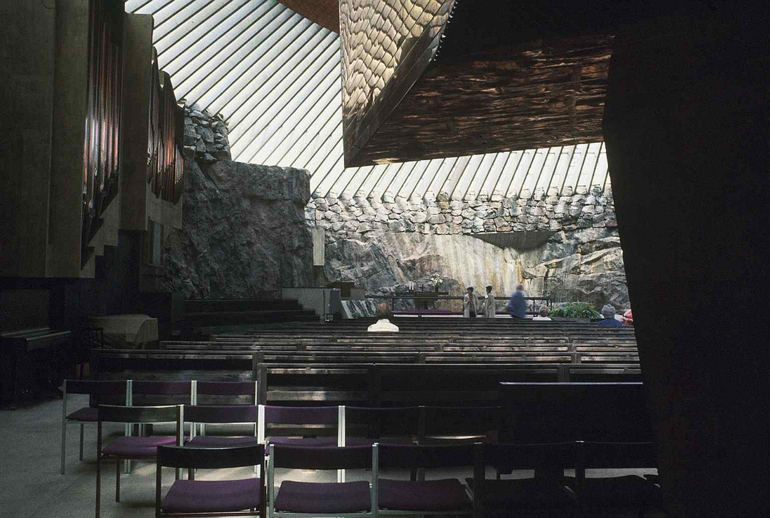The view from under the balcony shows the intimate oval hall, designed so the congregation feels surrounded by raw rock.