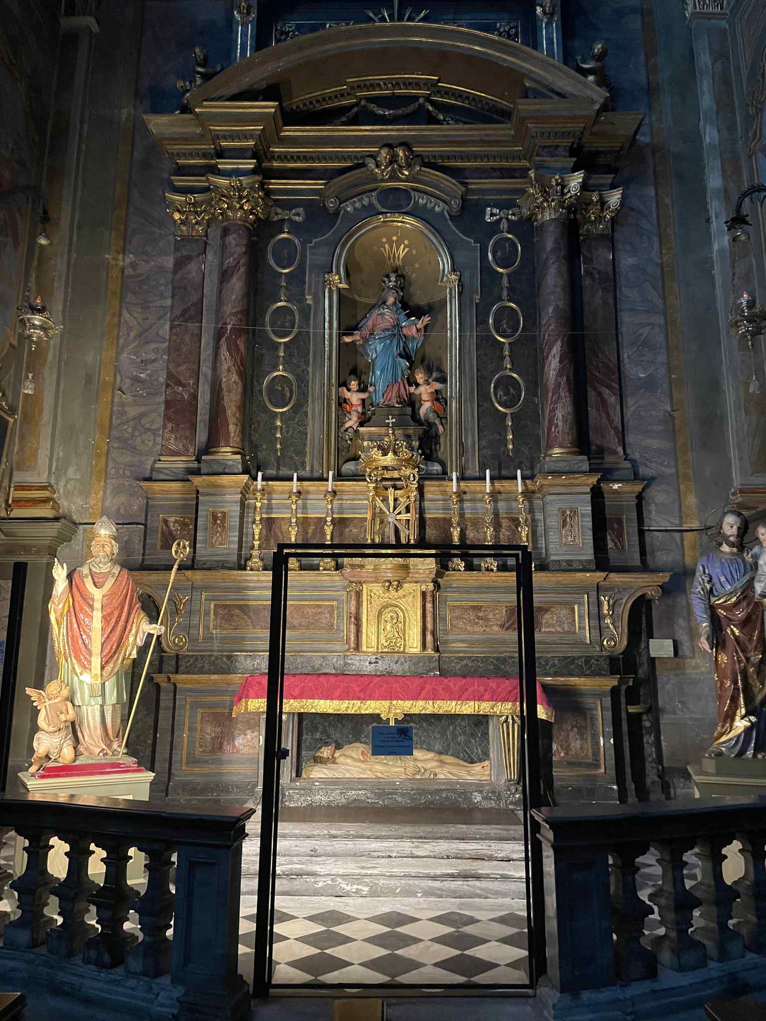Discover the altar of the crucifix, featuring a grandiose Neoclassical ancona with dark marbles, a striking crucifix, and a canvas of the Sacred Heart.