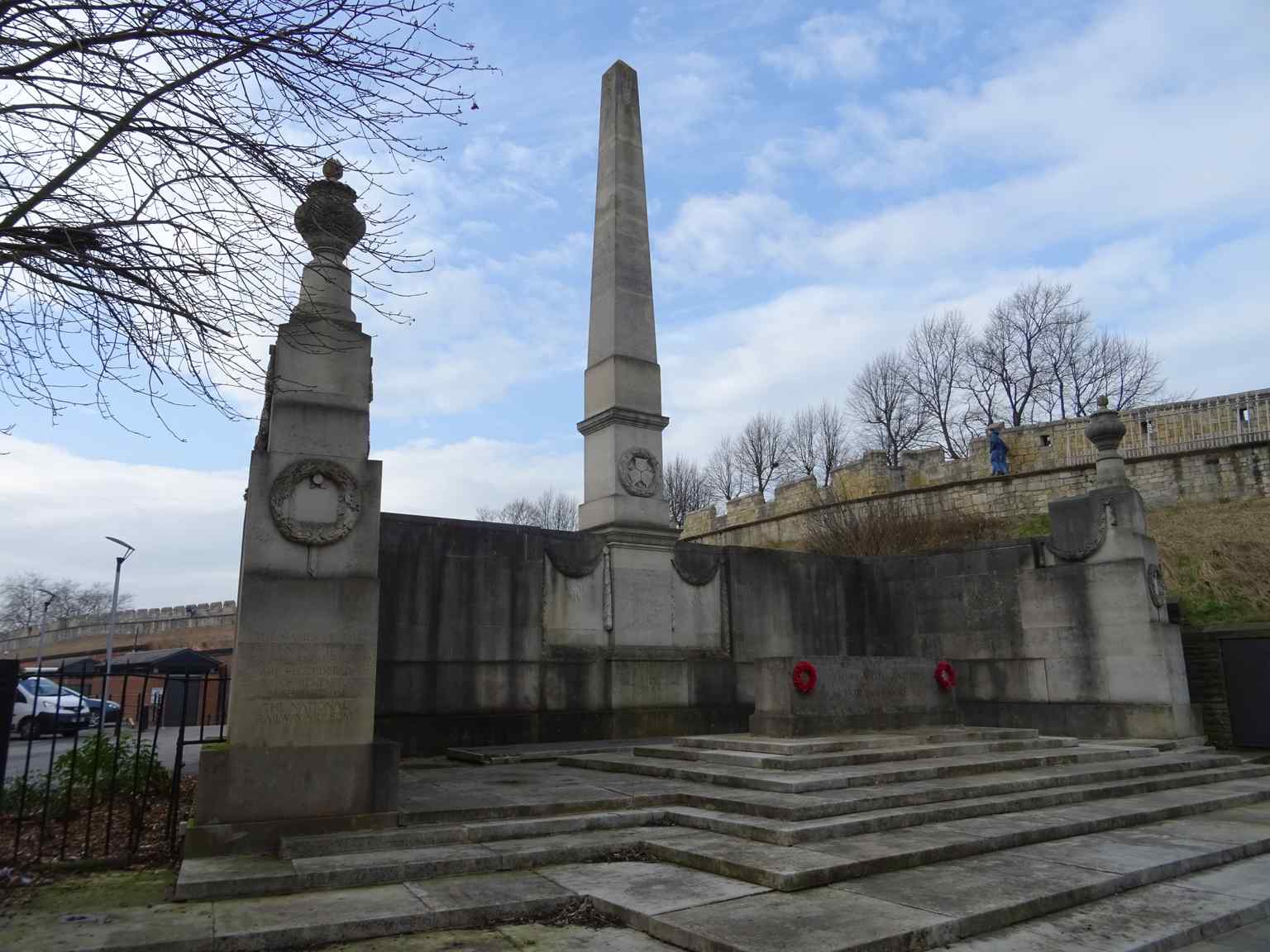 A full view of the North Eastern Railway War Memorial, standing tall with its central obelisk against the backdrop of the historic York City Walls (2017).