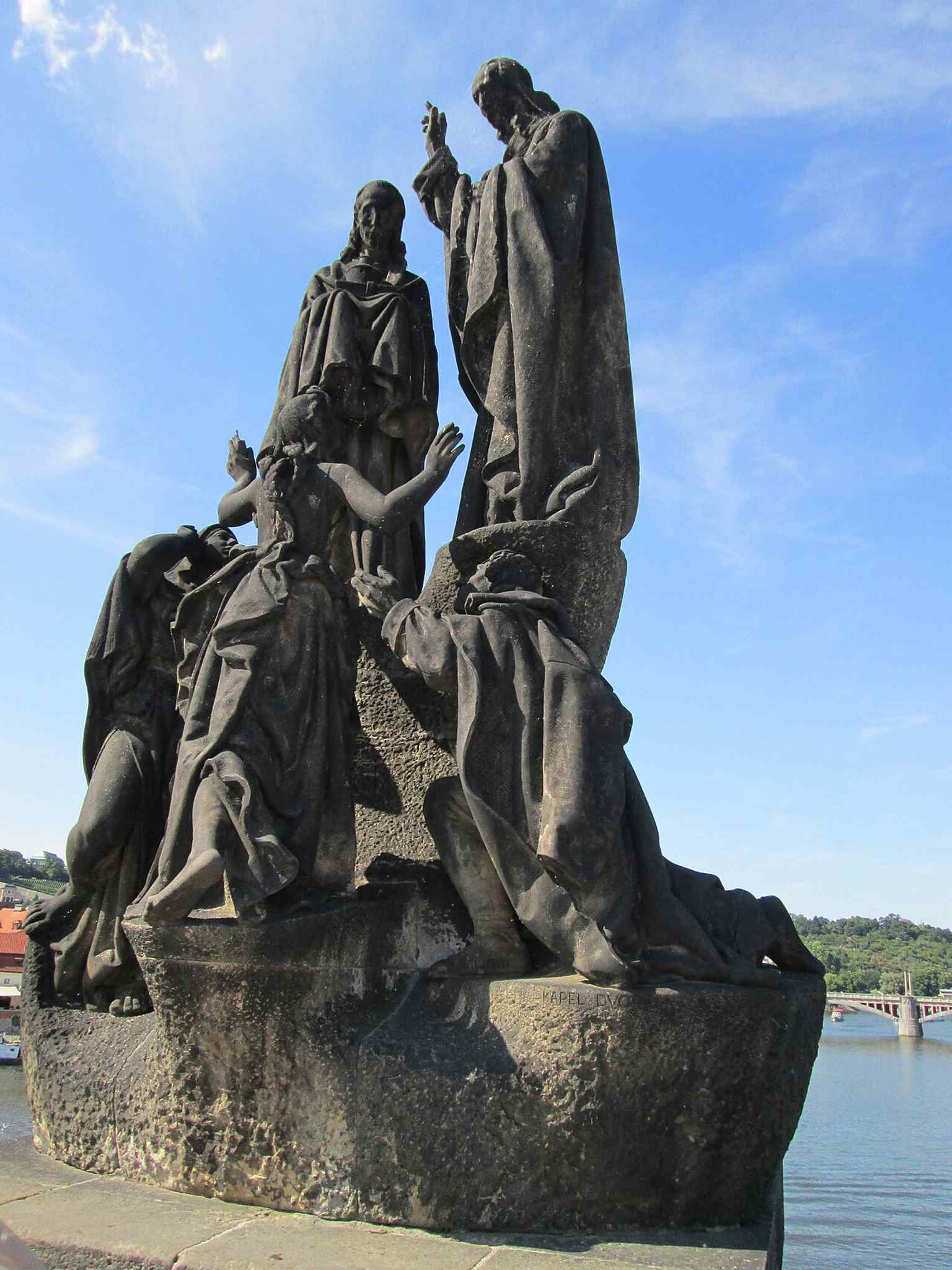The figures at the base, with outstretched arms, symbolize Bohemia, Moravia, and Slovakia, representing the nations of Czechoslovakia receiving the gift of faith and literacy.