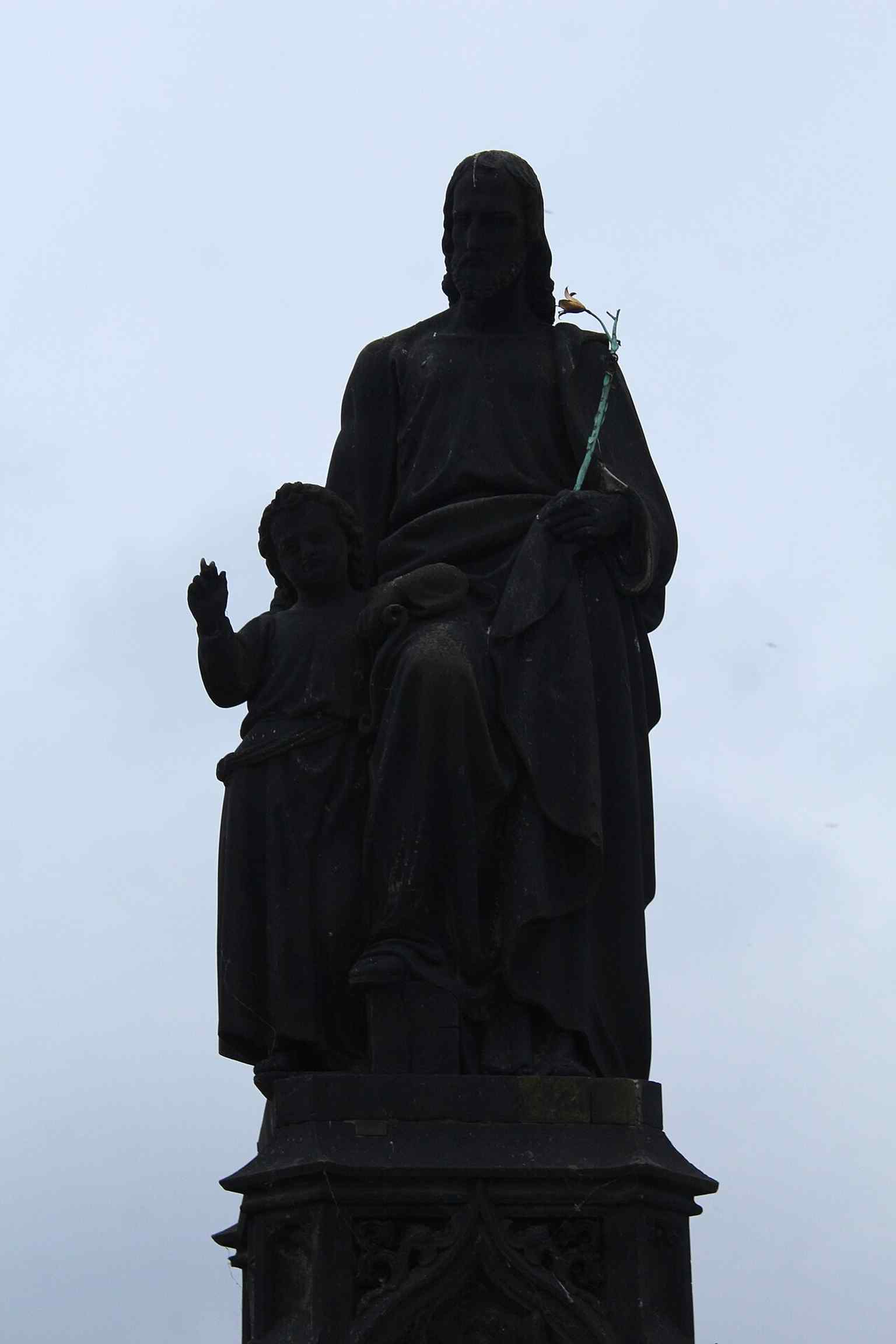 Josef Max's 1854 design for the current statue features a distinctively tall, pseudo-Gothic base, marking a stylistic departure from the bridge’s predominantly Baroque statuary.