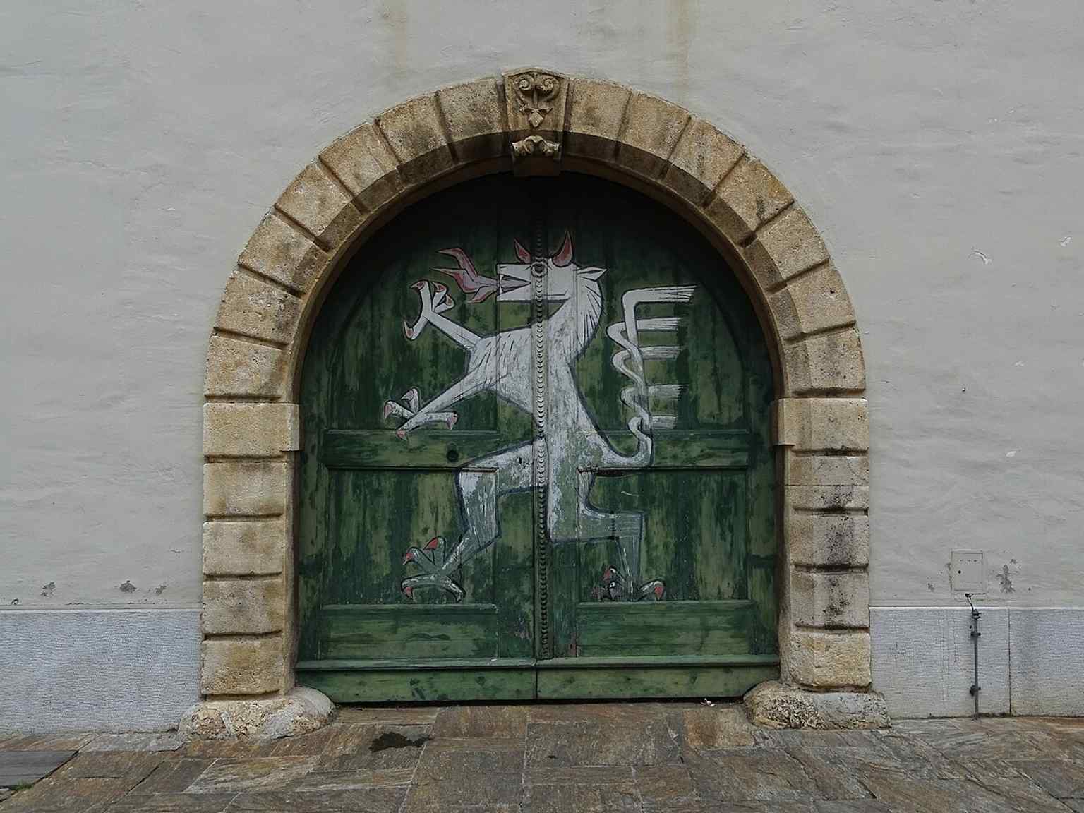 The steirischen Panther over a courtyard portal, a recurring regional symbol also mentioned in the building’s façades and roof details.
