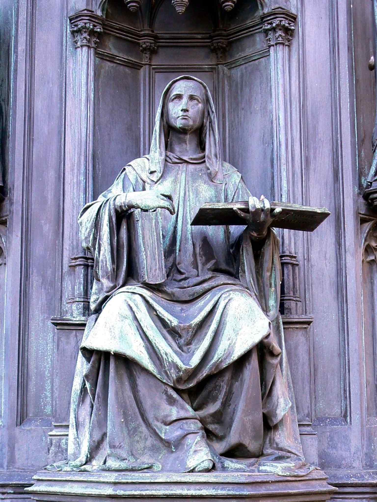 Representing the Faculty of Theology, this allegorical figure is one of the four seated statues adorning the statue's pedestal.