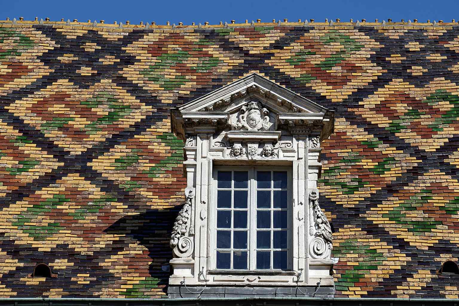 A close-up of the Hôtel de Vogüé's mosaic-like glazed tiled roof, a quintessential feature of traditional Burgundian architecture.
