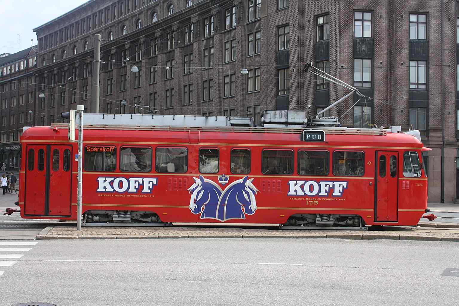A clear side view of the red Koff tram in service, matching the landmark’s signature look with the 'PUB – Kiertoajelu' concept.