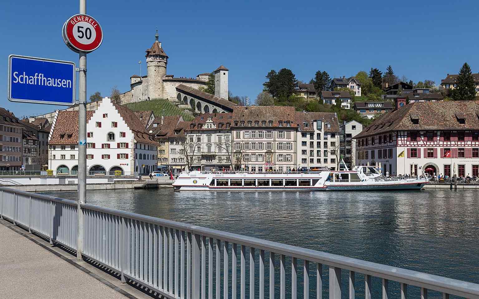 A broad riverside view with Munot in the background, showing the bridge’s place on the city edge where the Rhine forms both a border and a crossing.