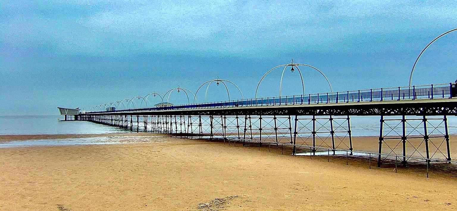A cropped perspective that emphasizes the long, straight run of the pier over the beach and reclaimed land.