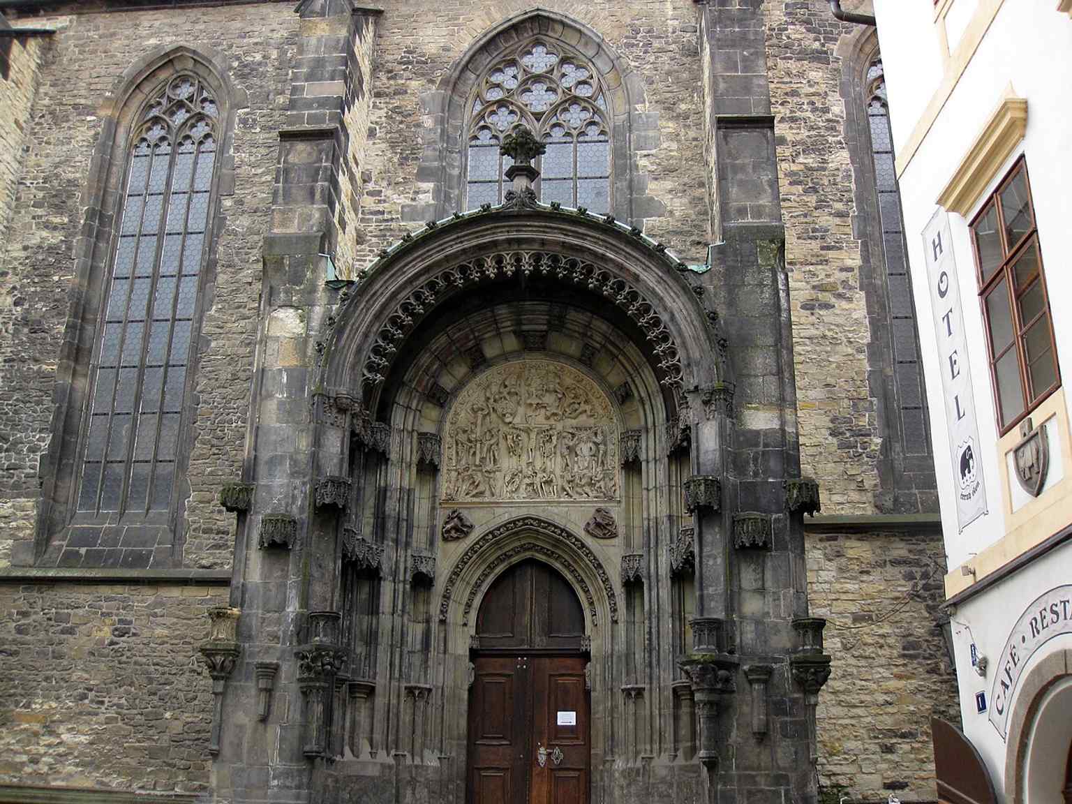 Das prächtige Nordportal zeigt ein prachtvolles Tympanon mit Szenen aus der Passion Christi, ein bedeutendes Beispiel vorhussitischer gotischer Bildhauerei, das von der Werkstatt Peter Parlers beeinflusst wurde.