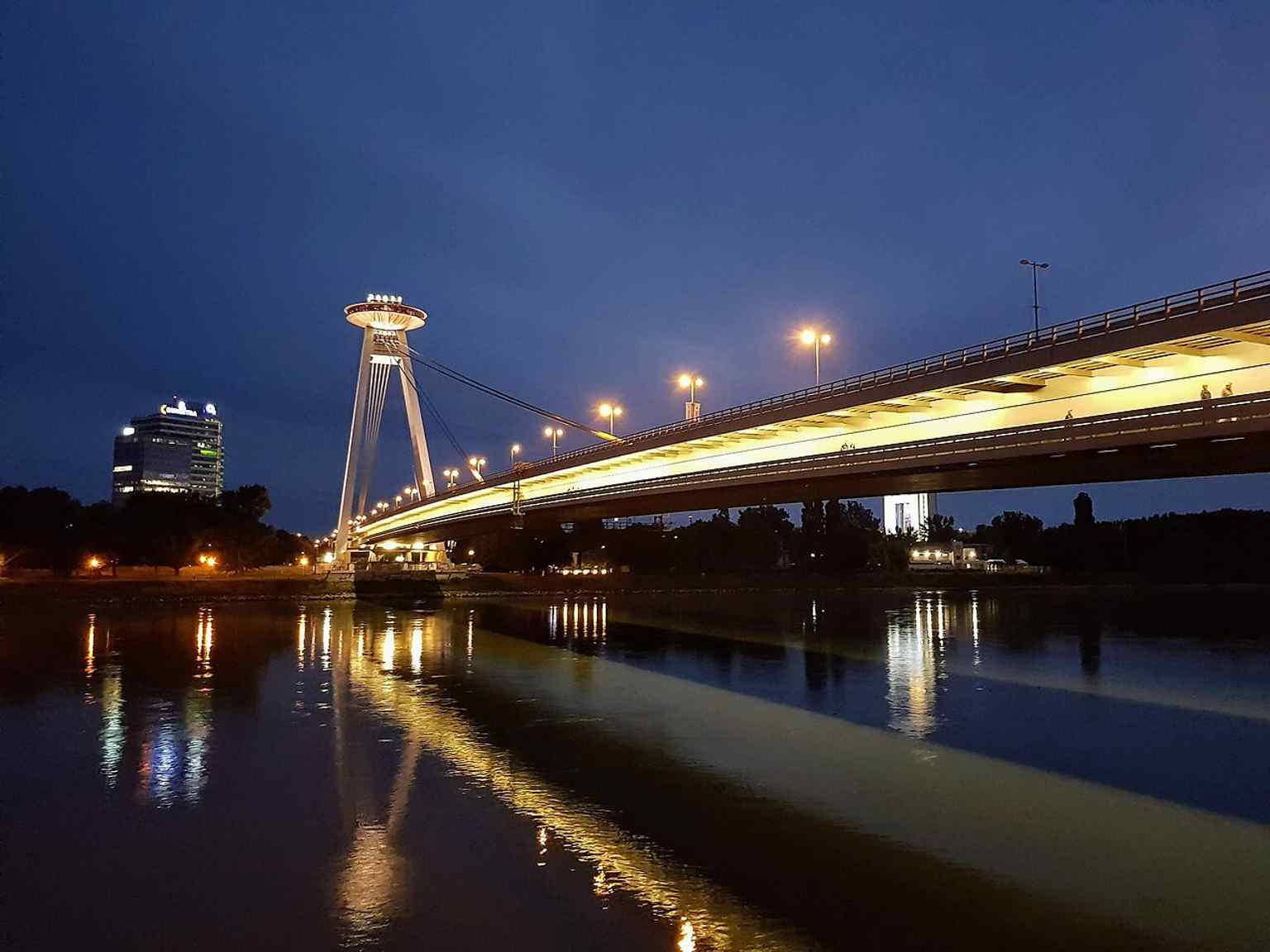 Night view with blue-hour reflections — a dramatic look at the illuminated bridge and its UFO-topped pylon.