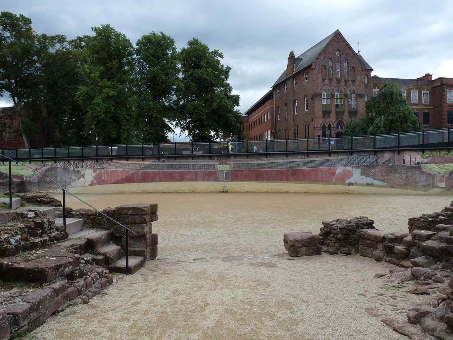 View south from the arena entrance down the steps, highlighting the sunken arena level and the modern access route into the ruins.