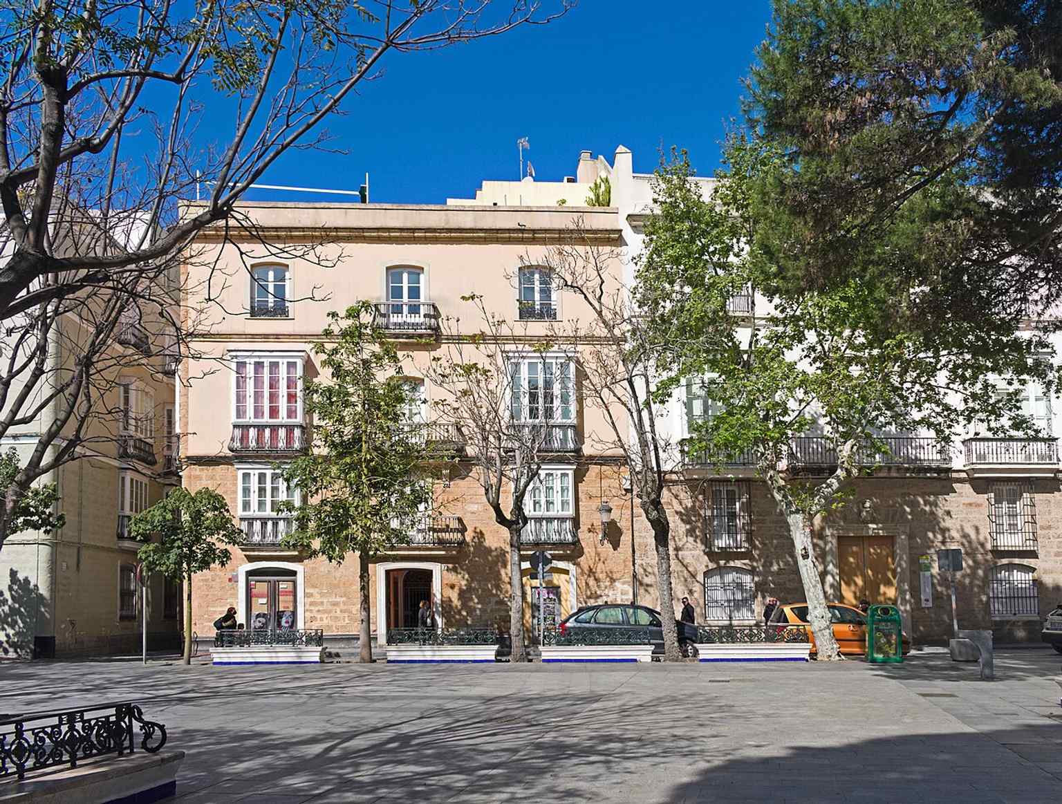 A street-level view of Plaza de Mina in Cádiz, the historic square created in 1838 on former Franciscan orchard land and later reshaped around its central garden.