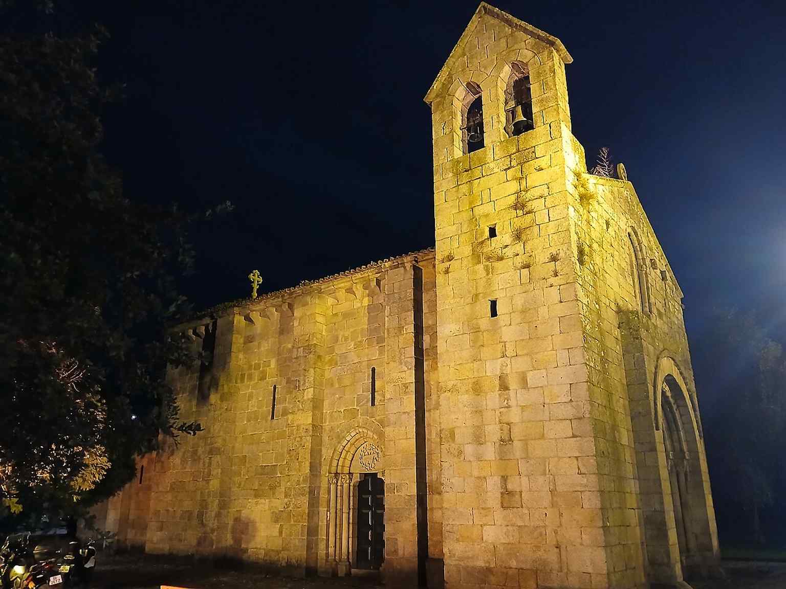 A night view of the church’s left side, where the heavy buttresses and narrow Romanesque windows reveal the single-vaulted medieval structure.