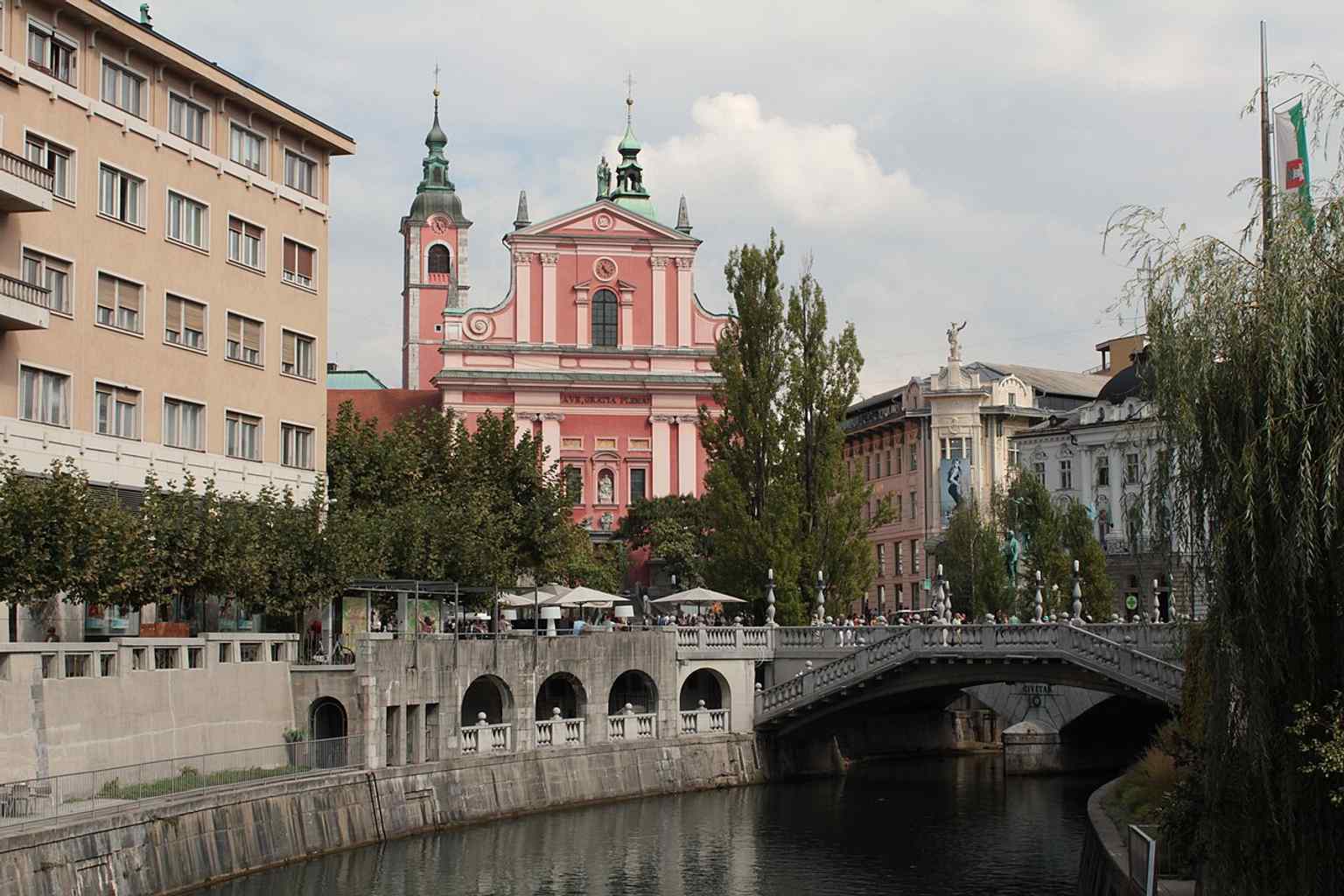 This image perfectly illustrates the Triple Bridge, designed by Jože Plečnik with its distinctive white balustrades, which extends Prešeren Square's functional and visual space across the Ljubljanica River.