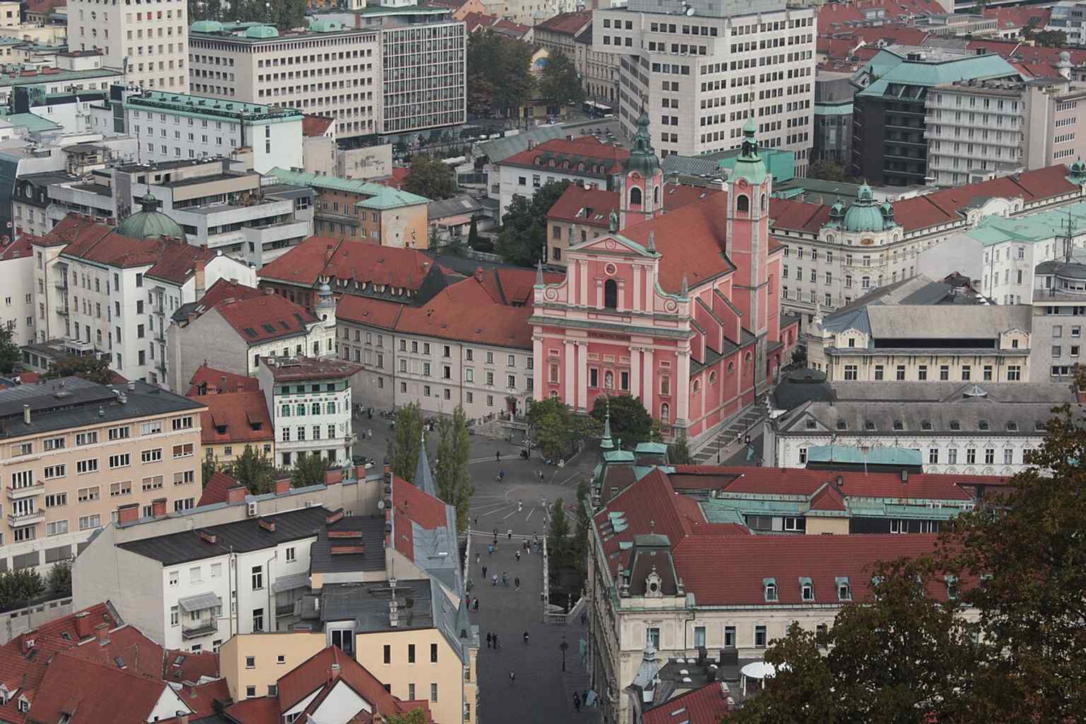 An aerial perspective from Ljubljana Castle reveals Prešeren Square's strategic location as a funnel-shaped crossroads on the left bank of the Ljubljanica River, opposite the medieval city center.