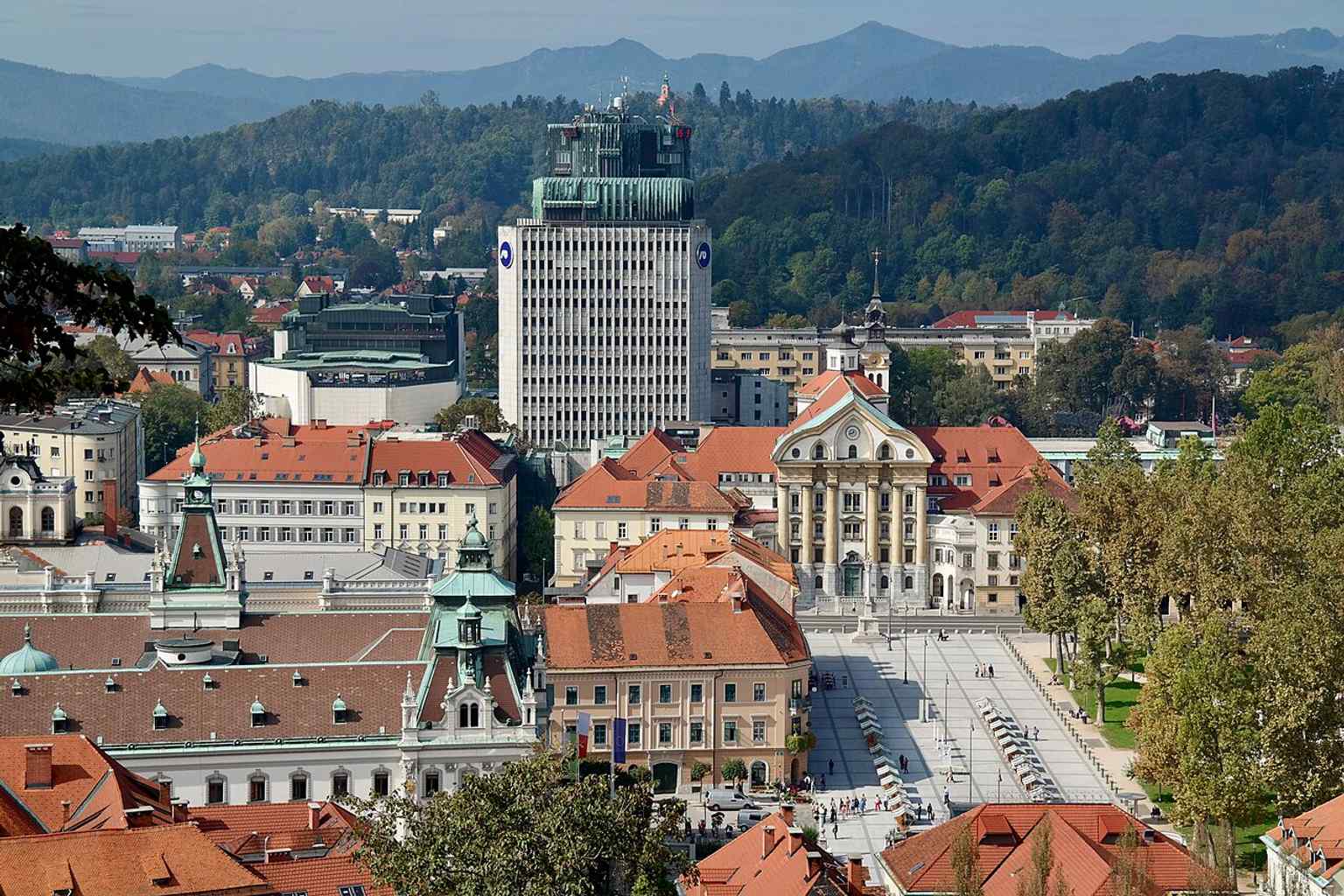 An aerial view of Republic Square from Castle Hill, featuring the distinctive brutalist TR3 and NLB towers. These buildings, part of Edvard Ravnikar's two-decade-long 'open planning strategy,' were originally envisioned as much taller 'Ljubljana gates'.