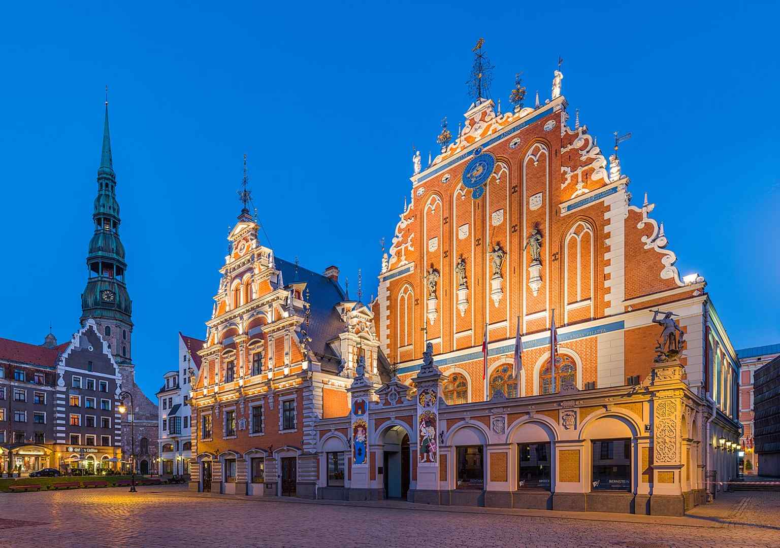 The House of the Blackheads beside St. Peter’s Church at dusk — a dramatic skyline view that places the landmark in Riga’s historic center.