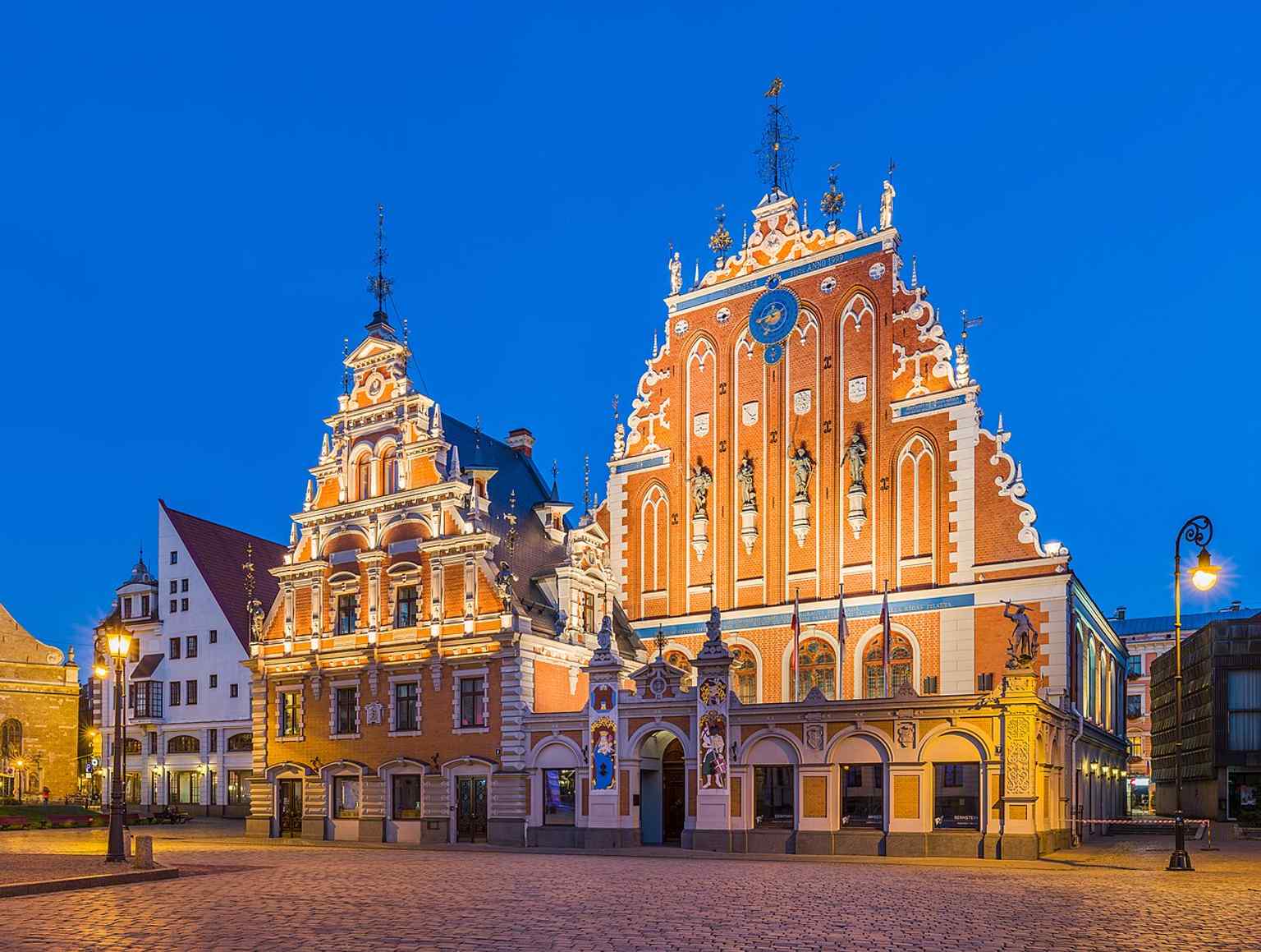 A warm dusk portrait of the façade, ideal for showing the building’s rich decorative gable and its prominent place on the square.