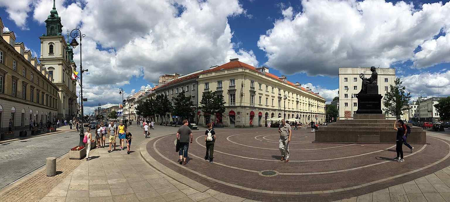 A broad streetscape of southern Krakowskie Przedmieście that situates the monument within Warsaw’s central historic axis.