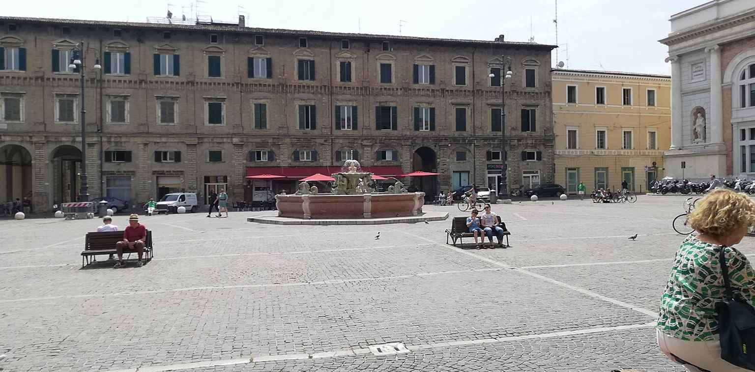 A broad view of Piazza del Popolo in Pesaro, where the square’s urban layout leads the eye toward its central fountain.