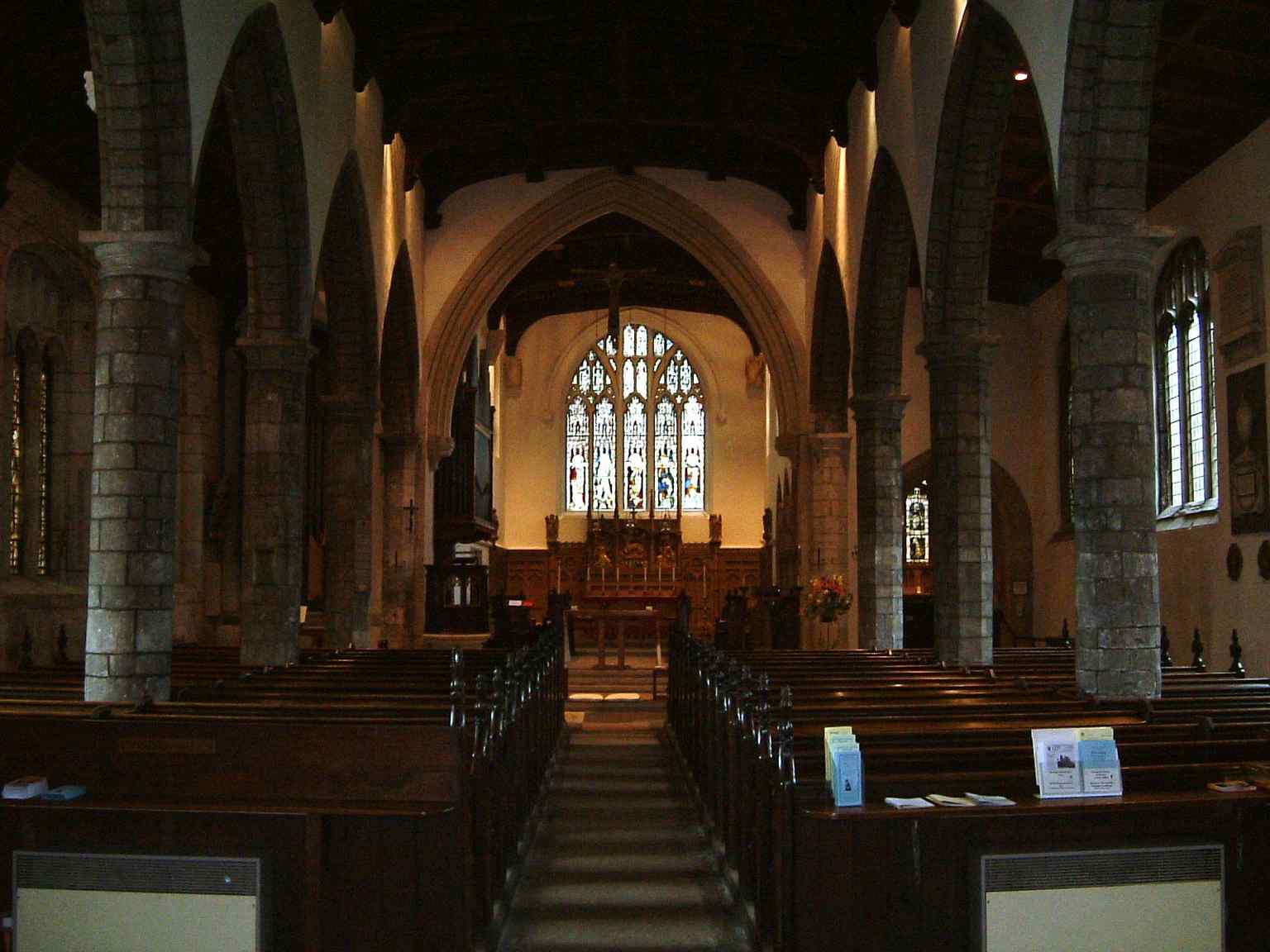 The impressive interior of Saint Olave's Church, featuring sturdy stone pillars and a brilliantly illuminated stained glass window at the far end (2005).