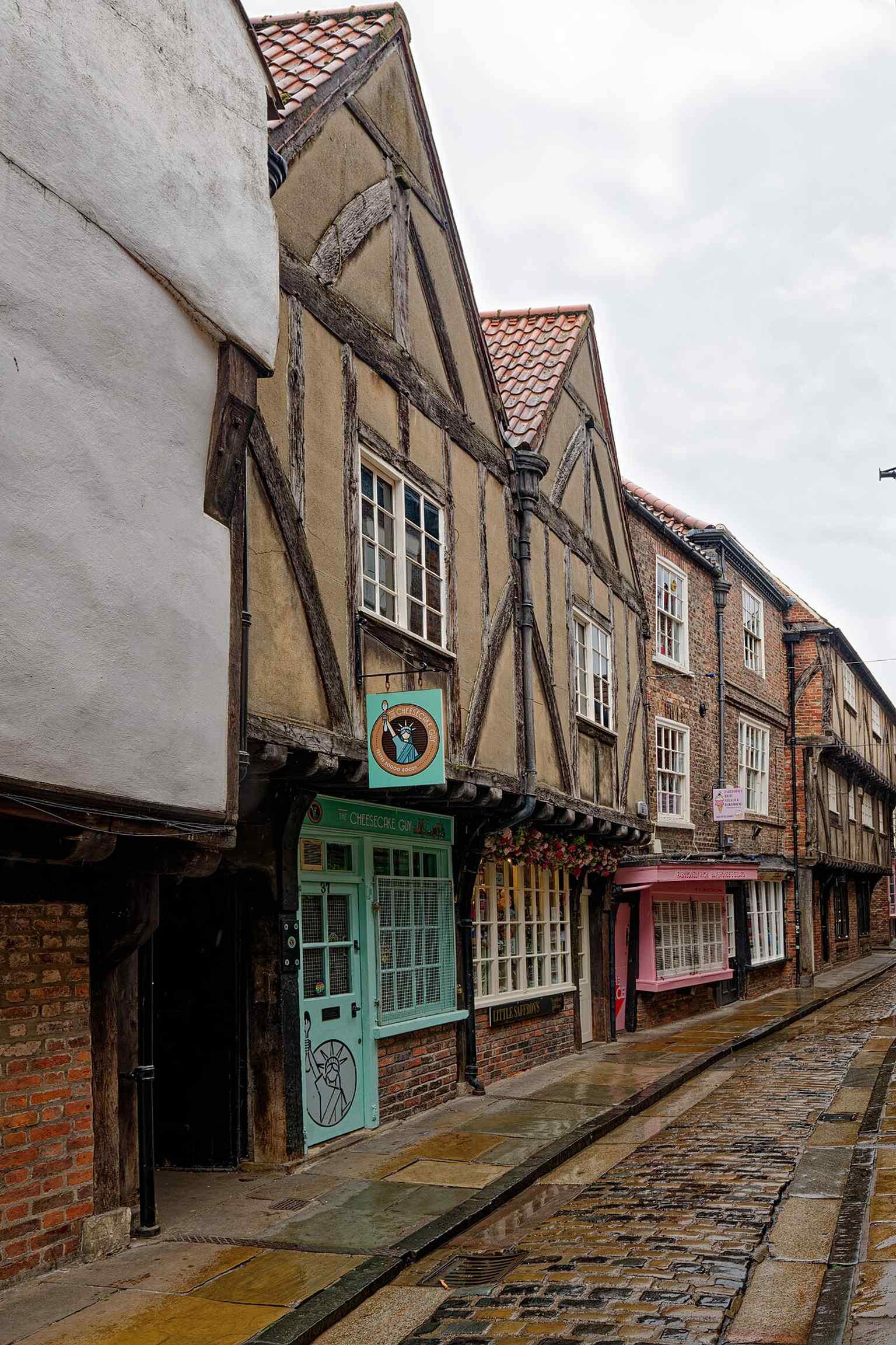 High-resolution view of the shopfronts at 37–38 The Shambles, showing how the medieval buildings now house modern businesses such as The Cheesecake Guy and Little Saffrons.