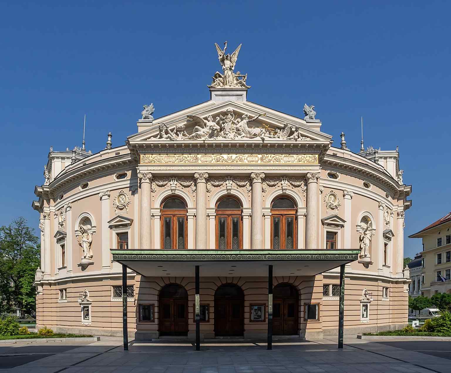 This image showcases the grand Neo-Renaissance facade of the Ljubljana Opera House, built between 1890 and 1892. Above the entrance, sculptures by Alojzij Gangl represent allegories of Tragedy and Comedy.