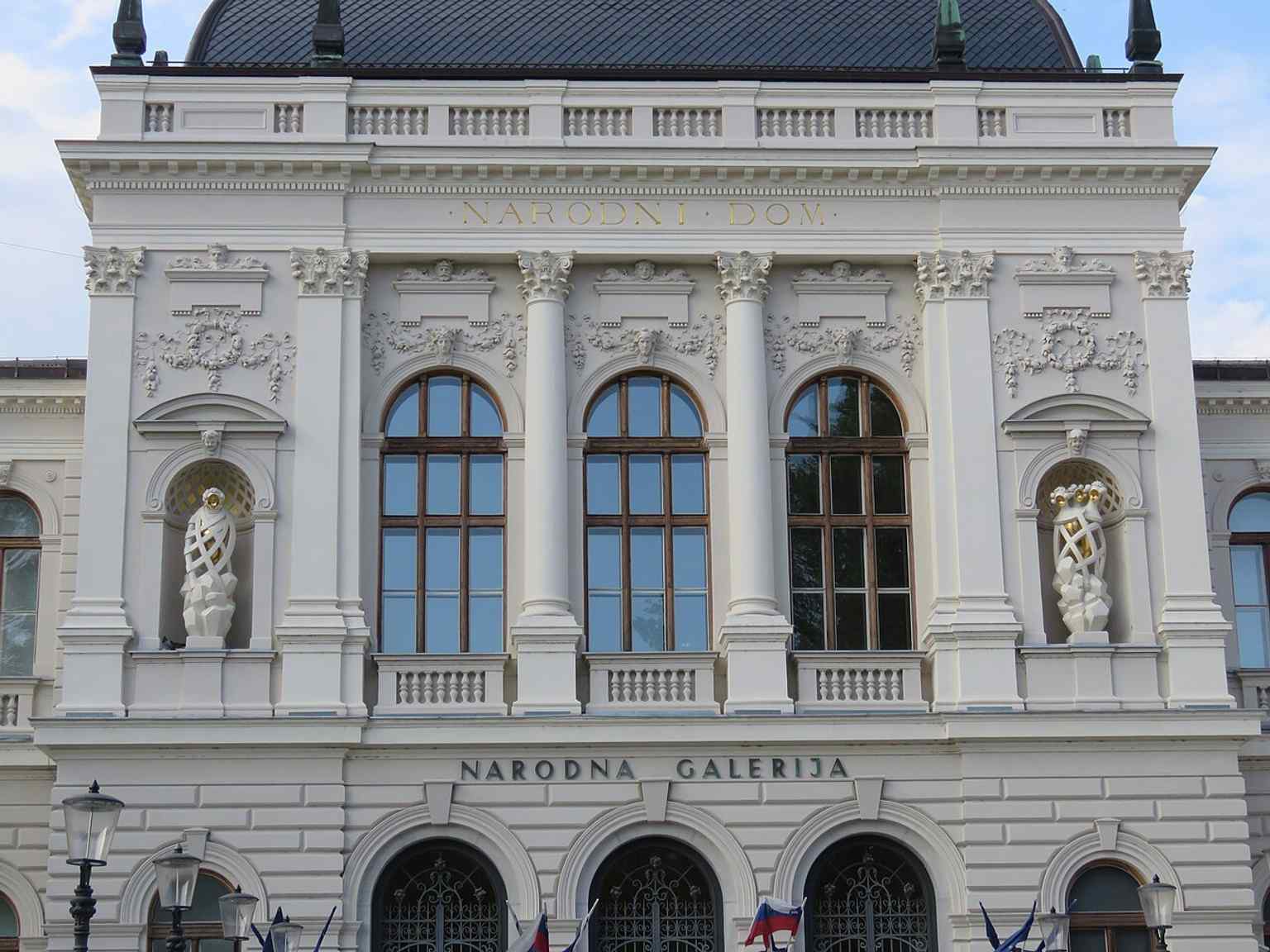 This image showcases the neoclassical facade of Narodni dom, whose niches were finally adorned with symbolic statues during the 2016 renovation, fulfilling architect Škabrout's original plans from 1896.