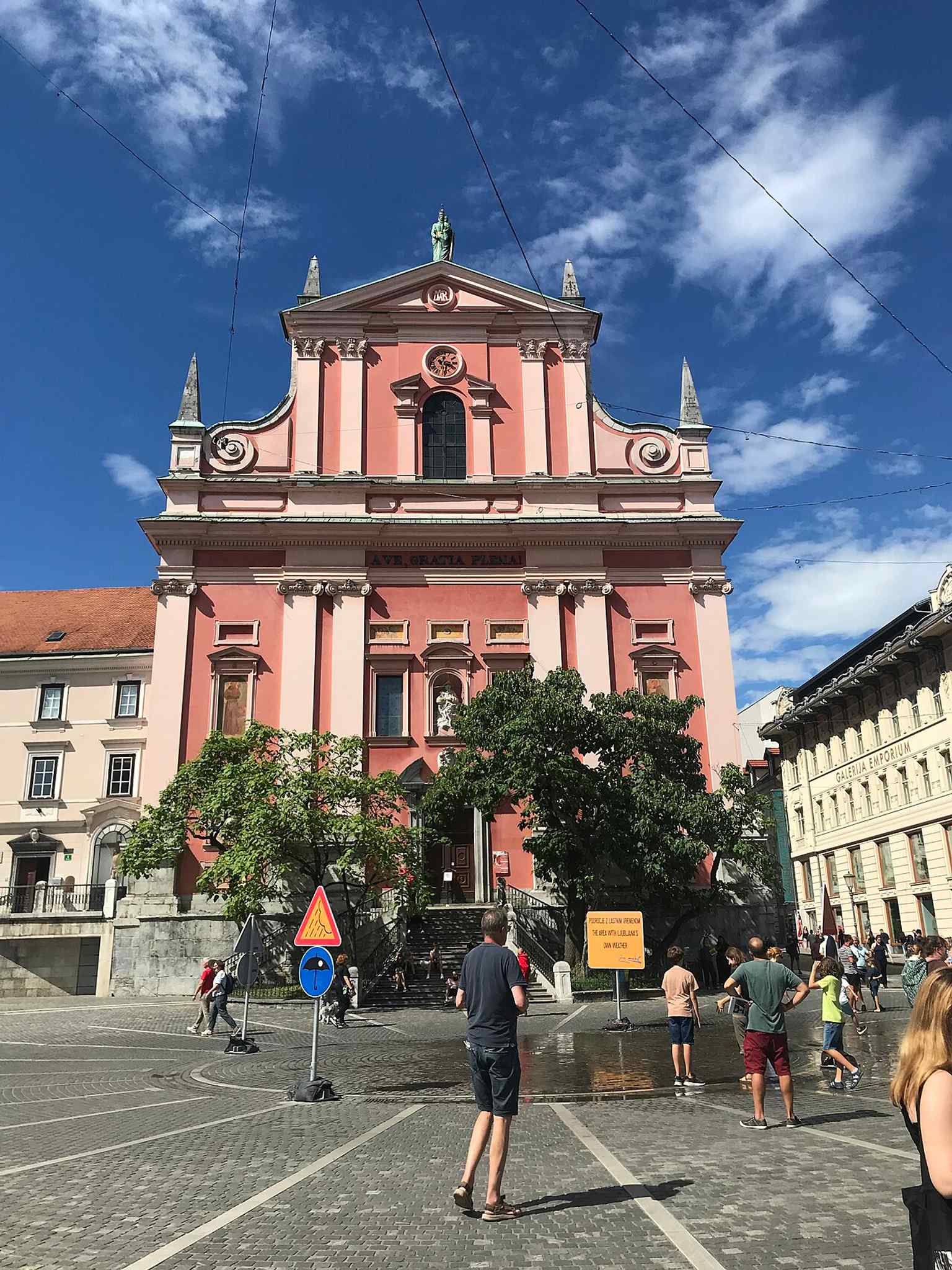 A vibrant view from Prešeren Square, showing the Church of the Annunciation, whose salmon-pink color represents the faded symbolic red of the Franciscan order.
