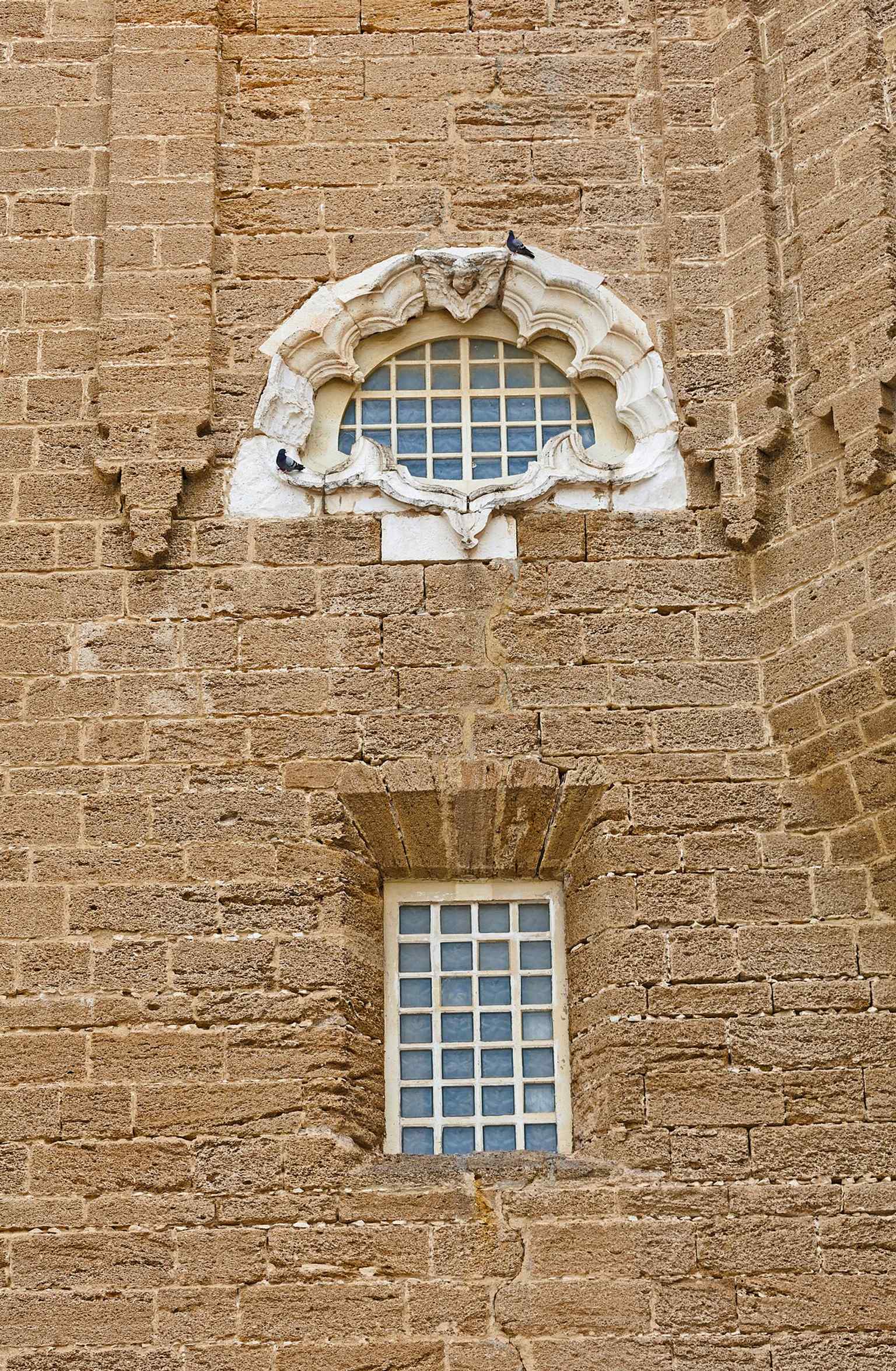 The west-side windows and exterior stonework, part of a building whose fabric has suffered from sea air and long restoration efforts.