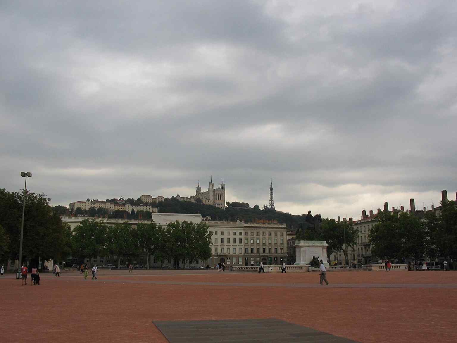 A classic daytime view toward Fourvière, capturing Bellecour as Lyon’s symbolic center with the hill rising behind the square.
