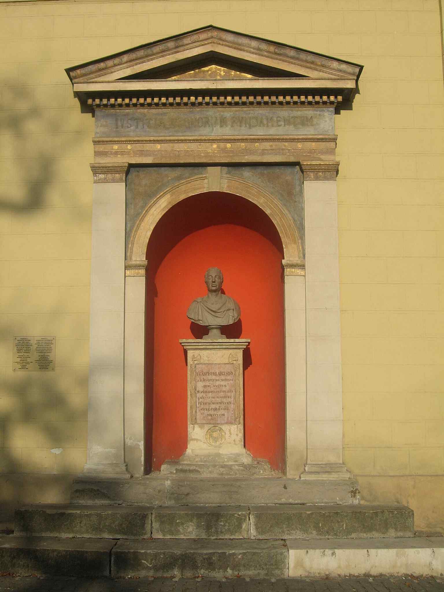 The classicist niche houses the bust, featuring columns, an entablature, and a triangular pediment, recalling ancient Greek monuments.