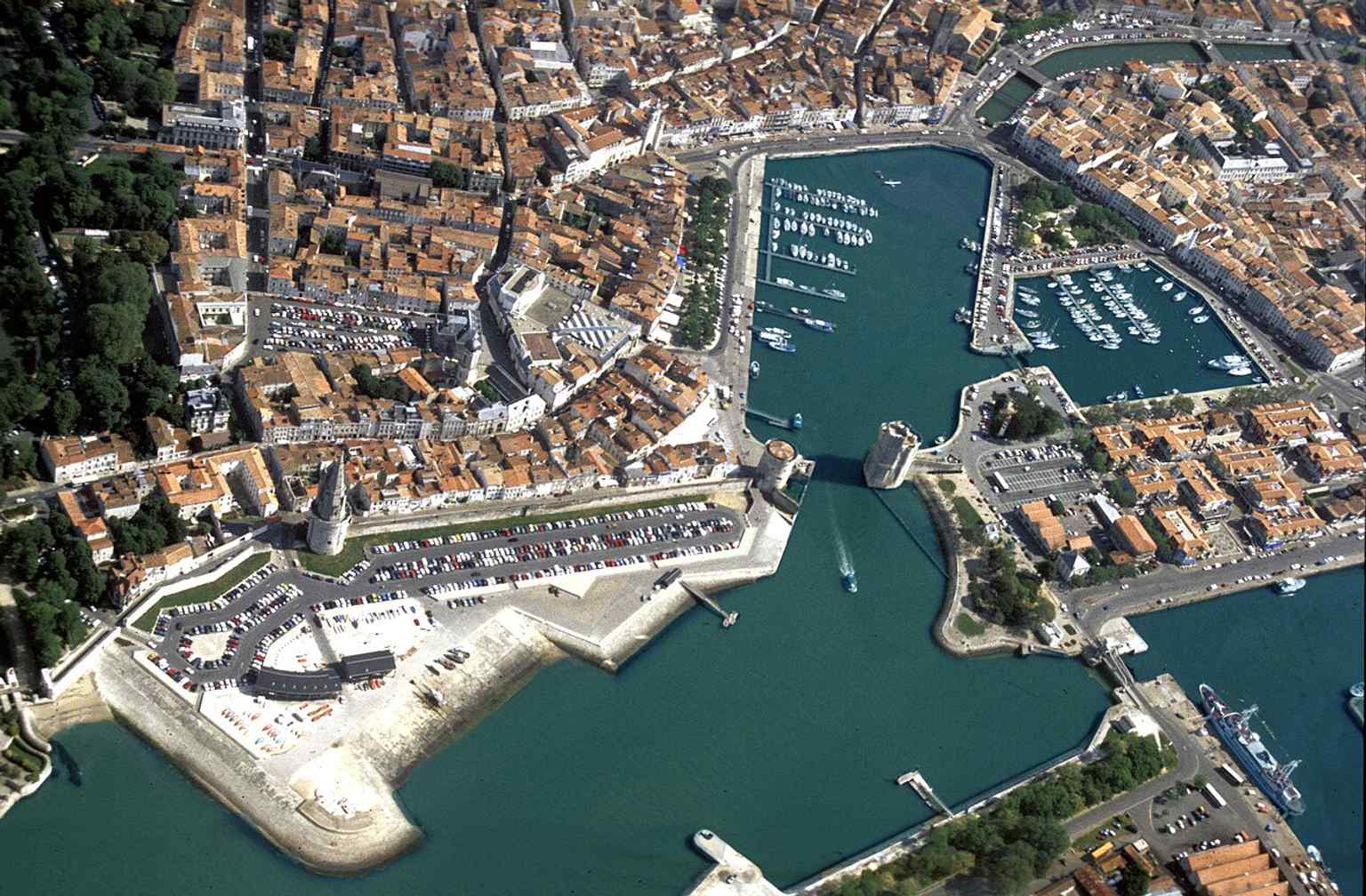 An aerial sweep of the Old Port showing the Saint-Nicolas, Chain, and Lantern towers together—the fortified entrance that once controlled access to the harbor.