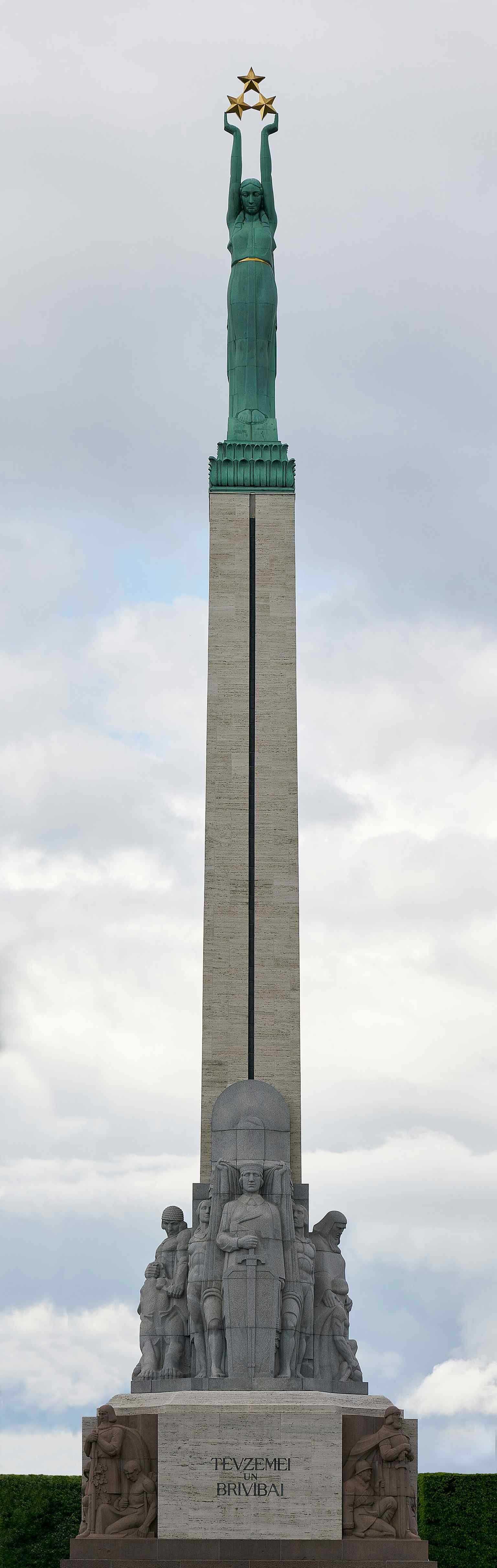 A full-height side view showing the monument’s stepped granite base and tall travertine column topped by Liberty and the three stars.