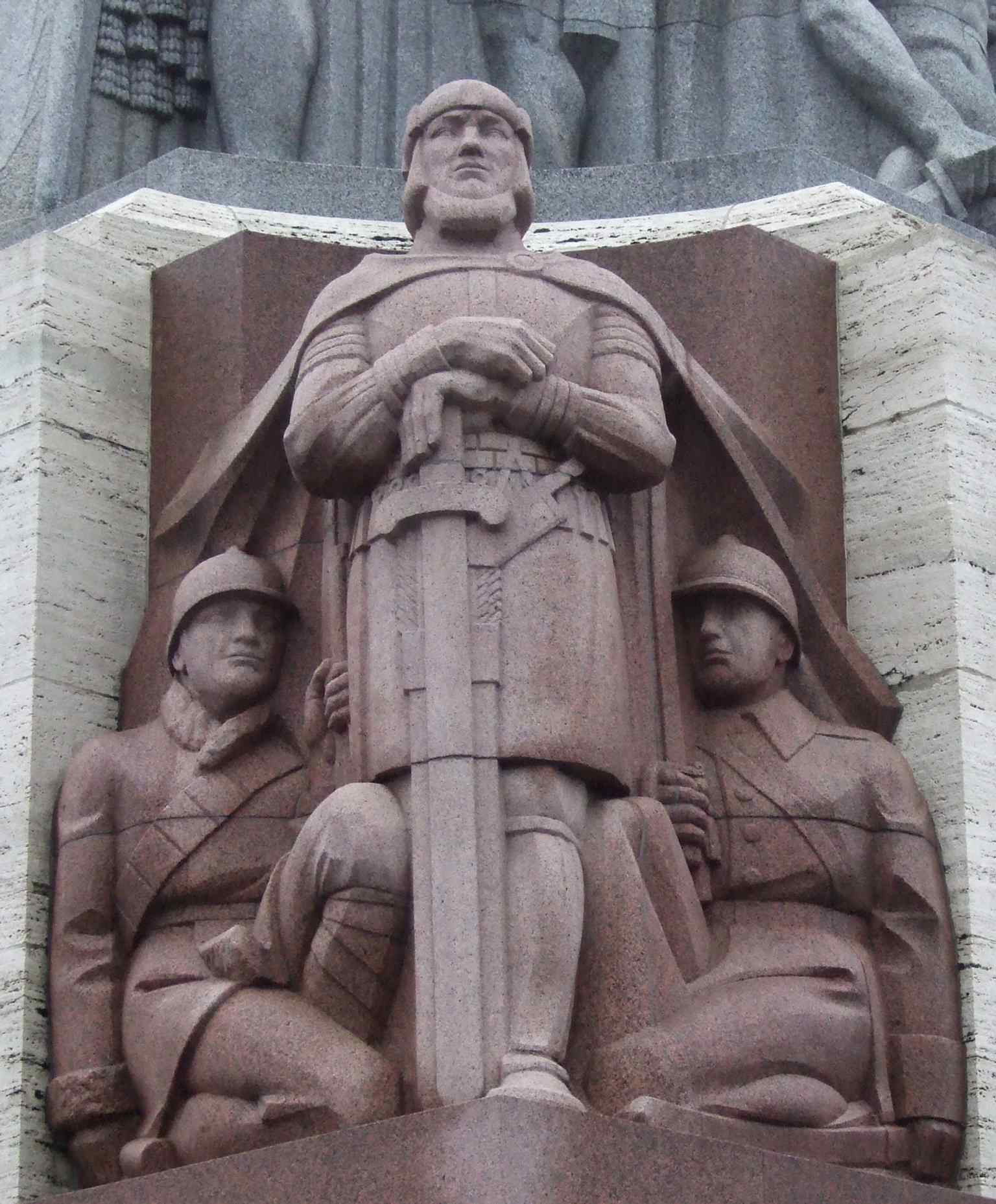 ‘Guards of the Fatherland’ depicts ancient and modern defenders together, linking Latvian history to the monument’s war memorial purpose.
