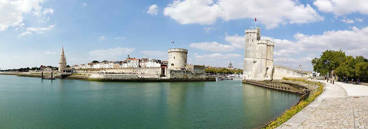 A wide panorama of the three towers of the Old Port, placing Saint Nicholas Tower in its full historic waterfront setting.